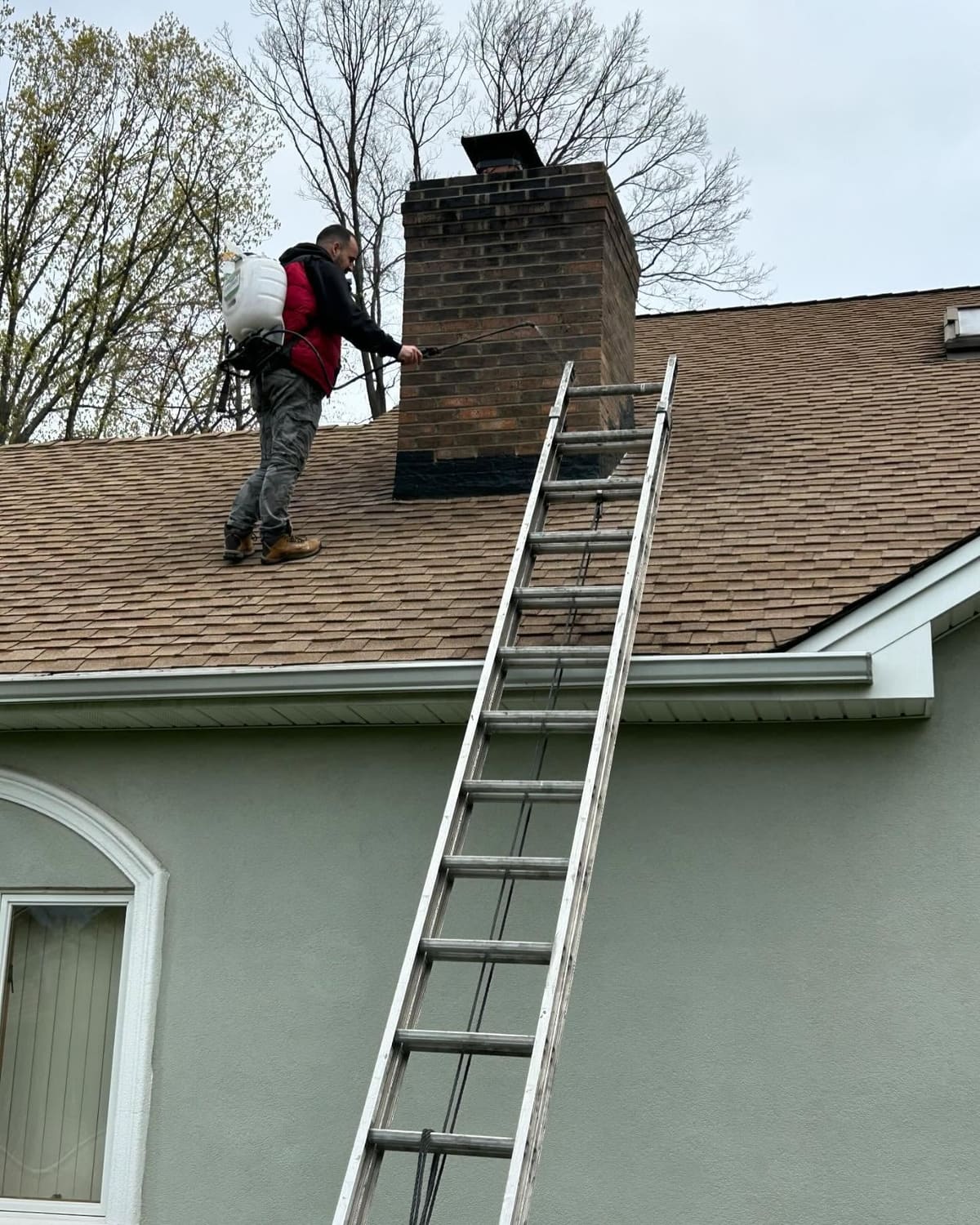 Technician on a ladder inspecting a brick chimney
