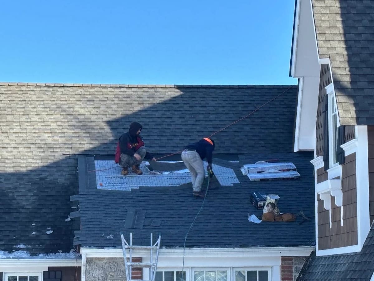 Roofers repairing a shingle roof section beside a dormer