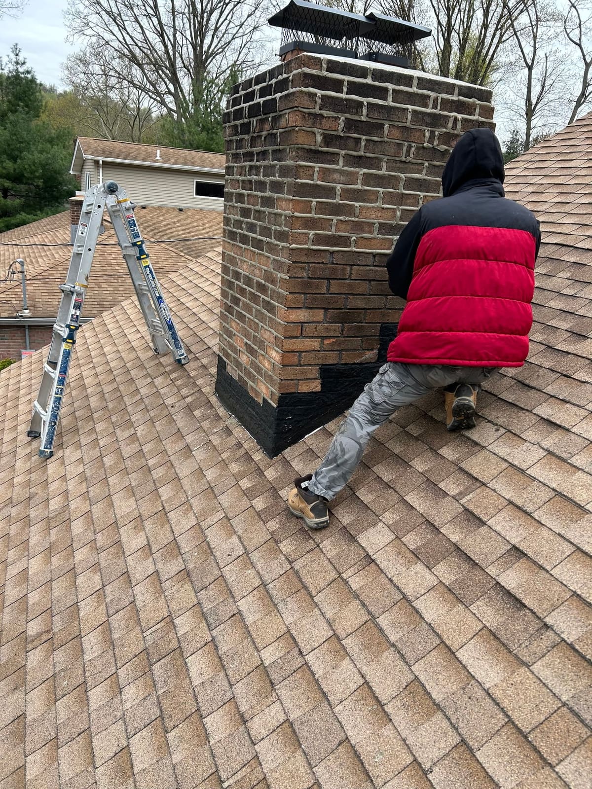 Roofer inspecting chimney flashing on an asphalt shingle roof
